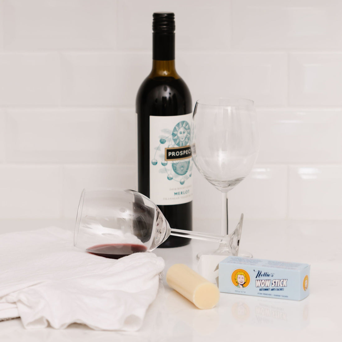 WOW Stick stain remover next to a bottle of wine and 2 glasses